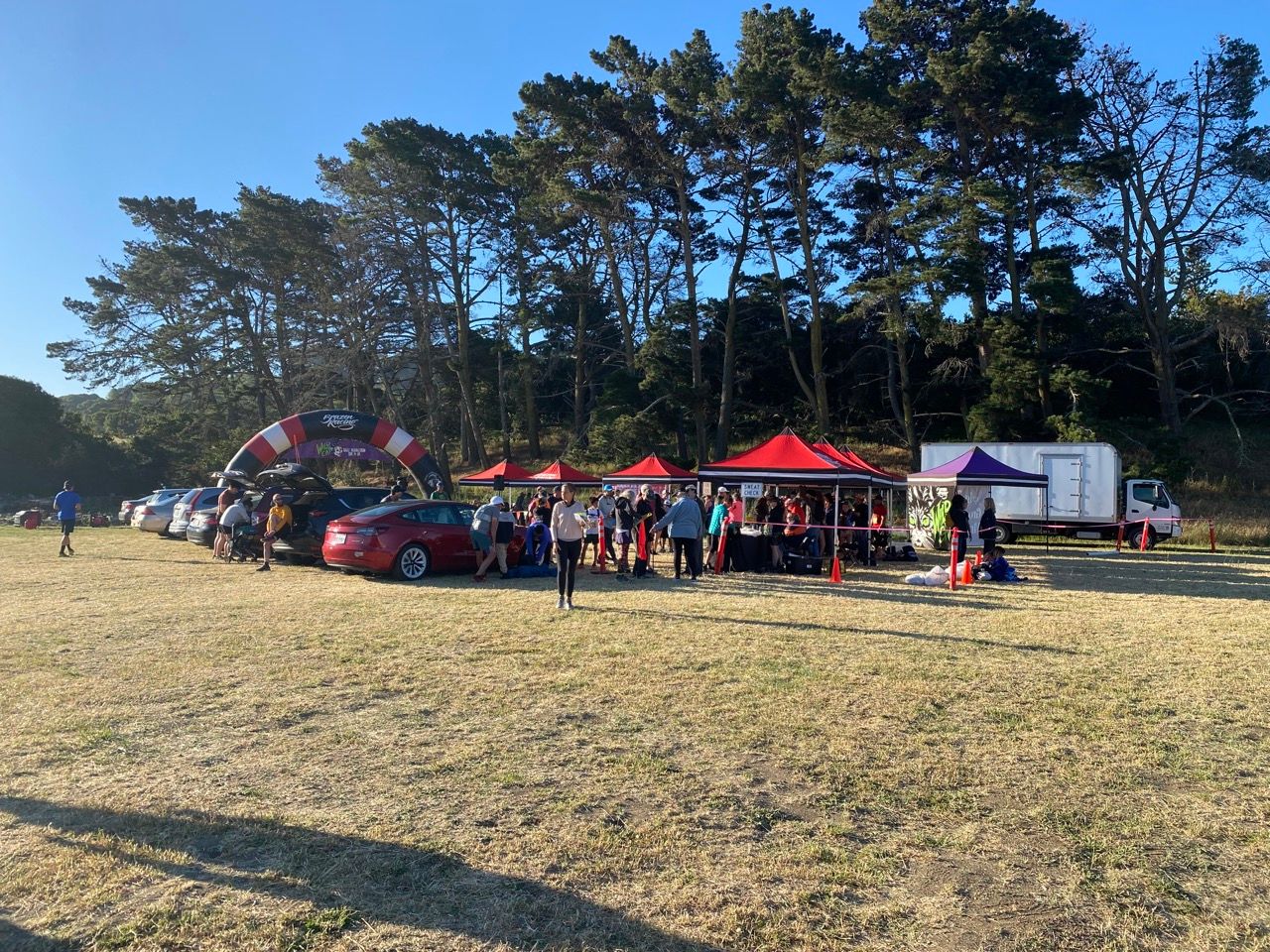 Running race starting village with red and purple pop-up tents and an inflatable finish arch, out in a field of dry grass.